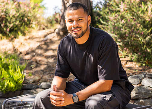 Man sitting, smiling on a bench outside.
