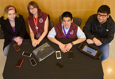 group of students sitting at table with cell phones and tablets