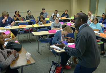 teacher speaking in front of students in classroom at desks