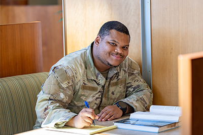 Davon Gray sits at a study booth in front of books, notebooks and pens; he is smiling at the camera and wearing army fatigues