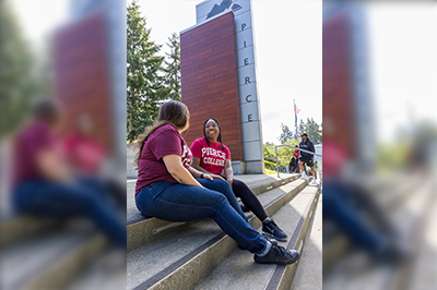 Students wearing Pierce College shirts sit laughing in front of the welcome sign at Pierce College Fort Steilacoom