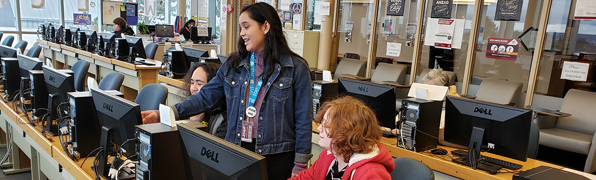 computer lab employee assisting two students at computers