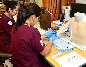 two nursing students in scrubs practicing with IVs